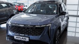 Geely Atlas бизнес кар у дилера в салоне сбоку спереди