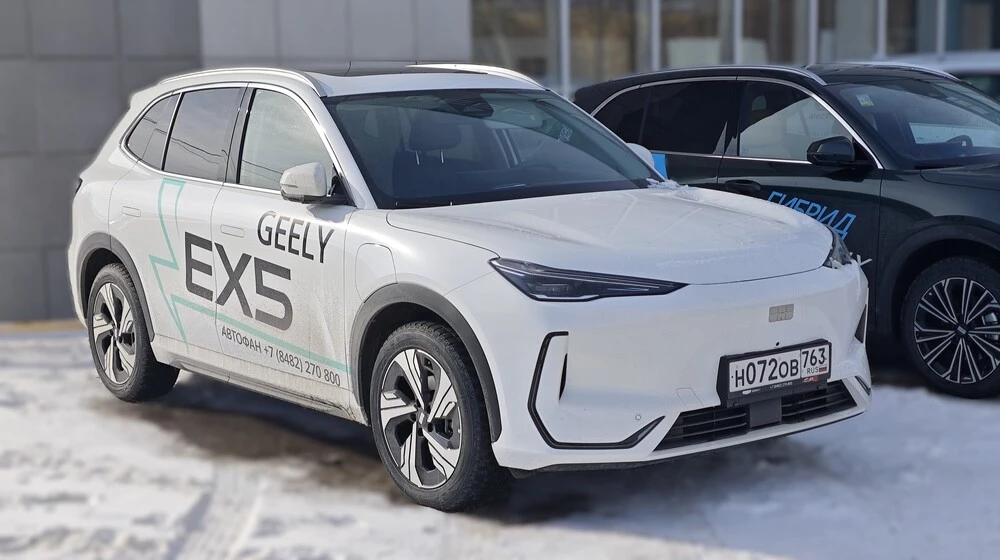 Geely EX5 сбоку спереди белый у дилера рядом автосалон